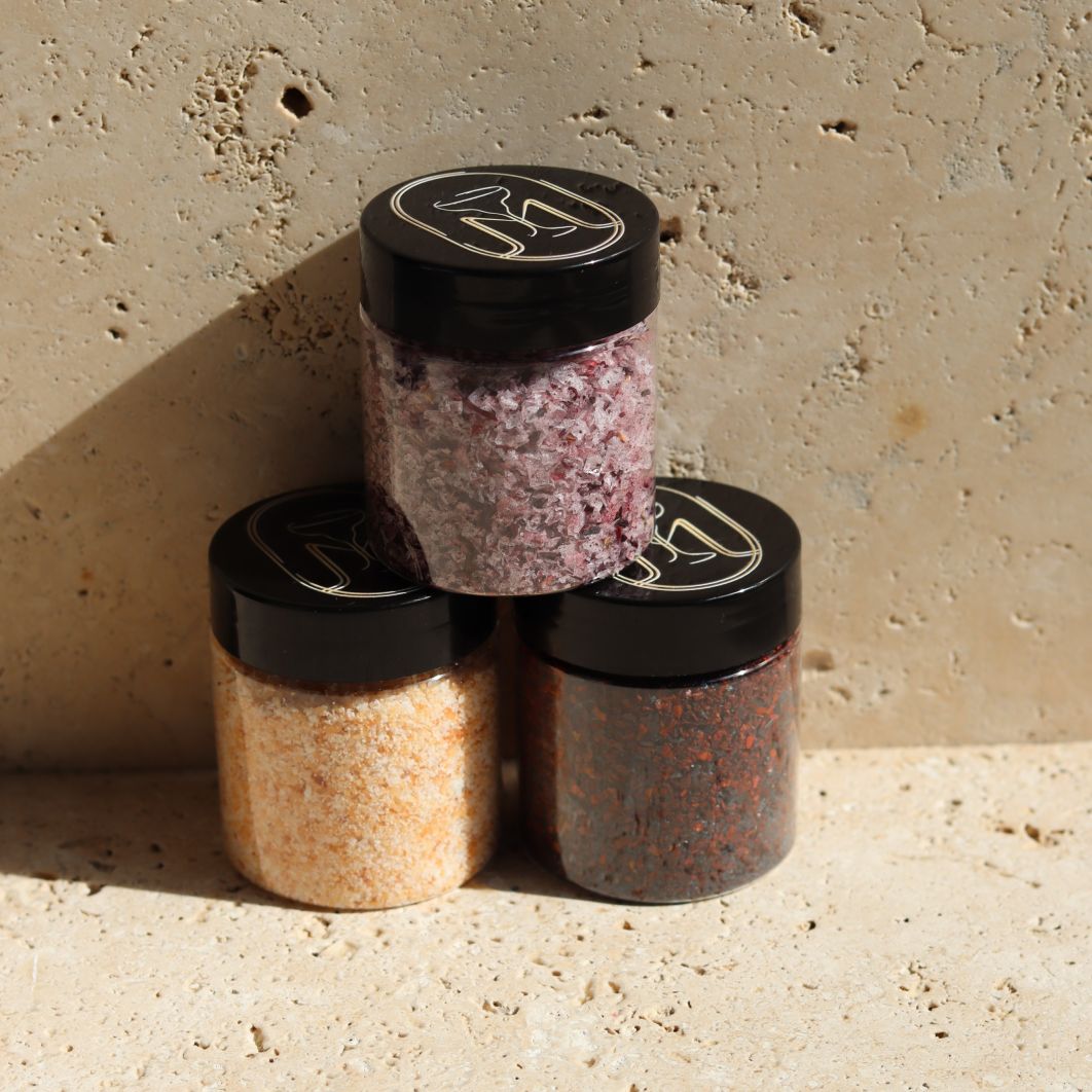 Three jars of different types of salt stacked on a stone surface with a neutral background
