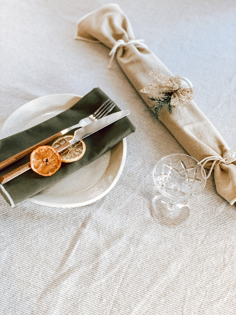 Table setting with a beige napkin, green napkin, and lemon slices on a white plate.