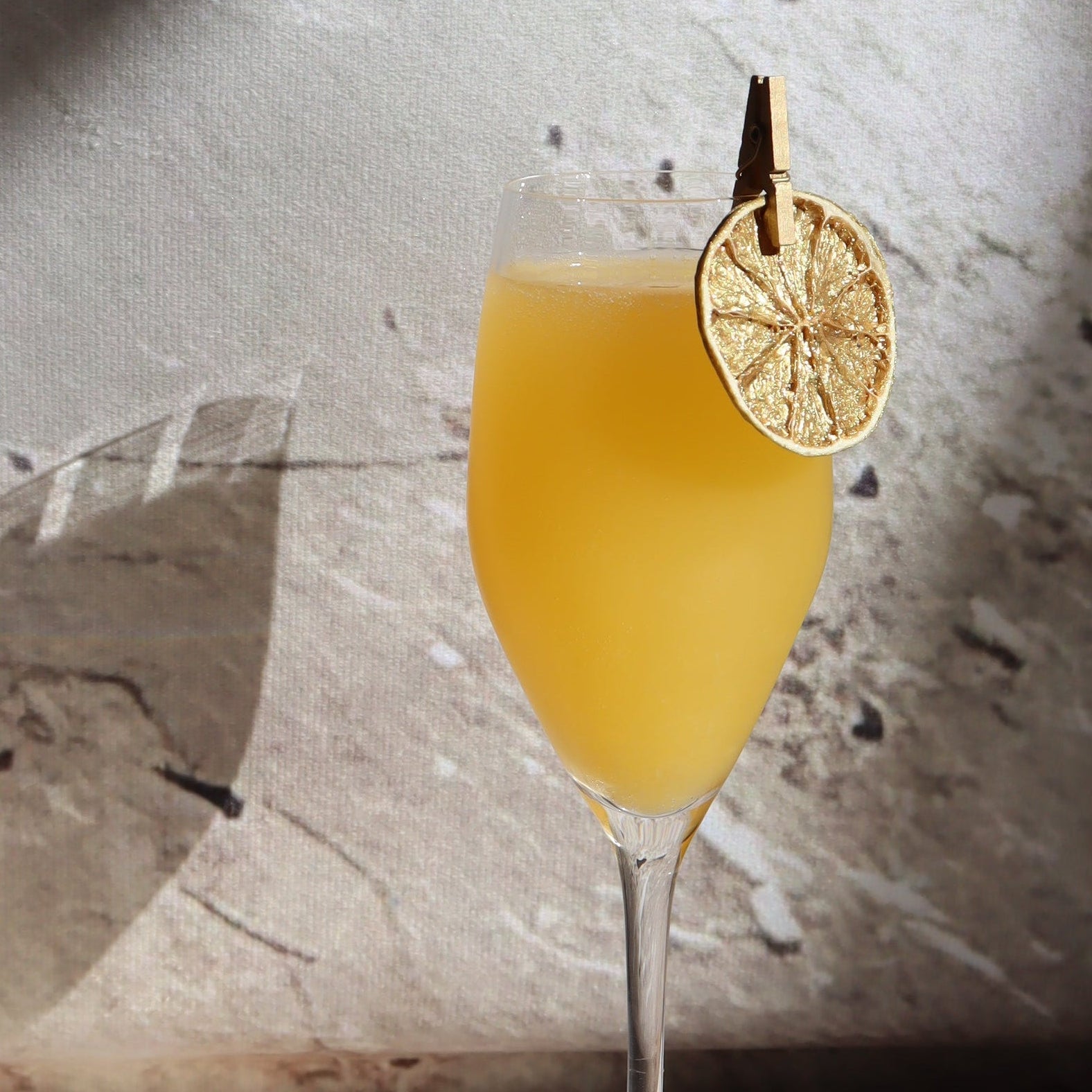 Mimosa cocktail in a glass and it's garnished with golden lime attached with a peg to the rim