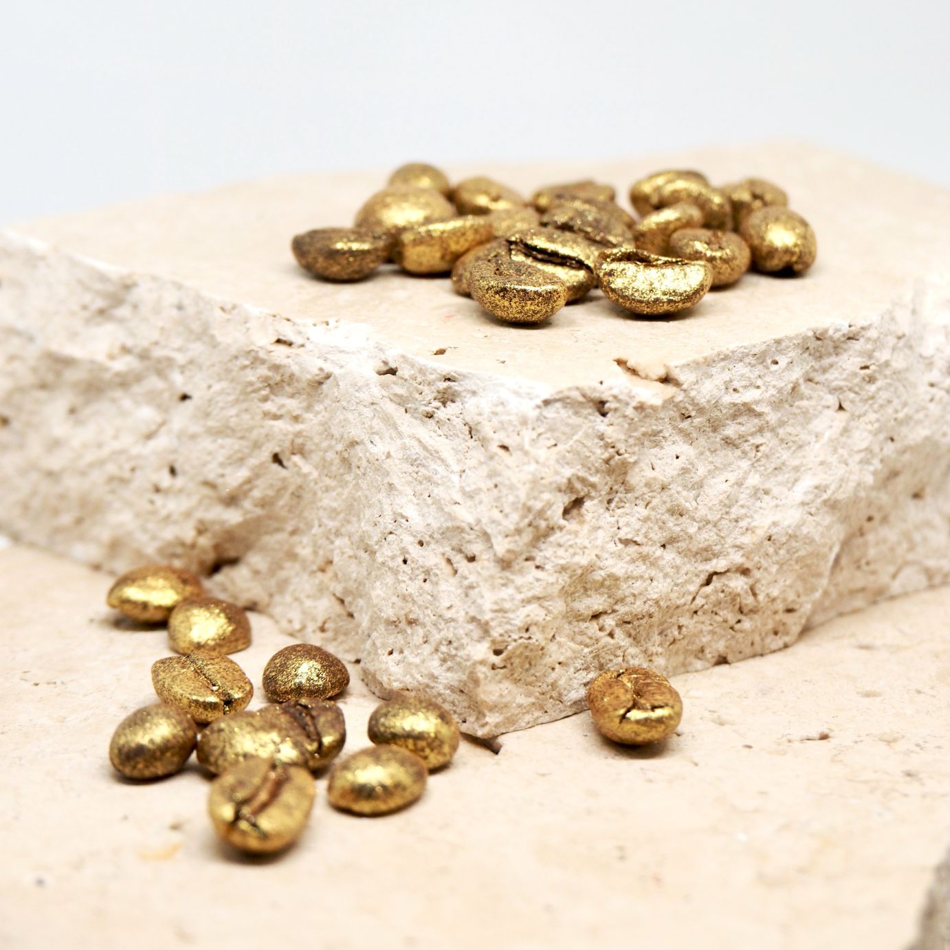 Gold coffee beans scattered on a travertine stone surface